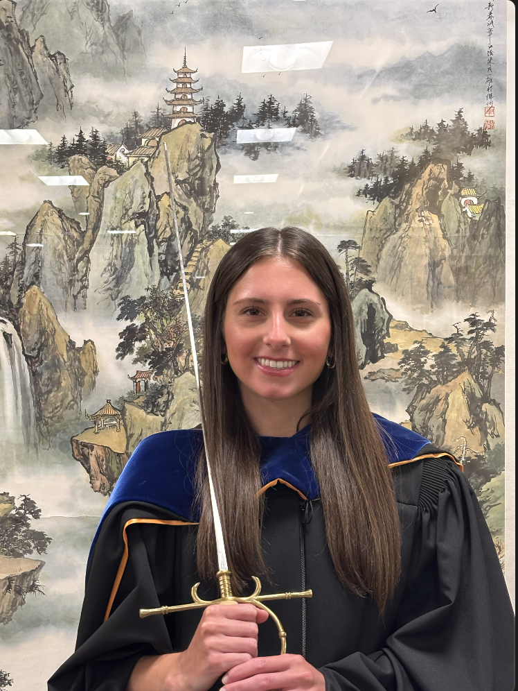 Professor Knoll stands in black before a painting and holds a rapier.